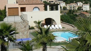 A pool area with lounge chairs, a stone wall, and a view of hillside buildings. - House / Villa - MONTICELLO (Monticello)
