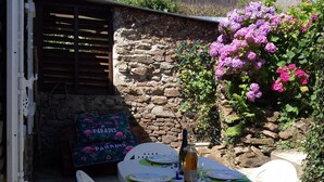 Une terrasse extérieure avec une table dressée pour deux personnes, entourée de chaises en plastique blanches, d’une bouteille de vin et d’un panneau décoratif.