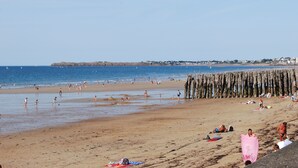 Une plage où des gens se prélassent au soleil et se baignent, un promontoire rocheux et un ciel dégagé.