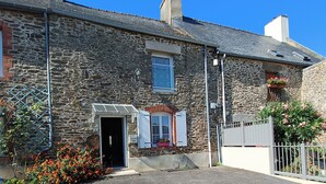 Un bâtiment en pierre avec une allée gravillonnée, une petite entrée et une fenêtre avec des volets.