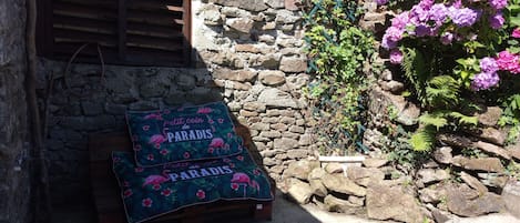 Een rustieke stenen muur met een houten bankje en een tafel, overdekt met een deken met de tekst 'Petit coin de PARADIS'.