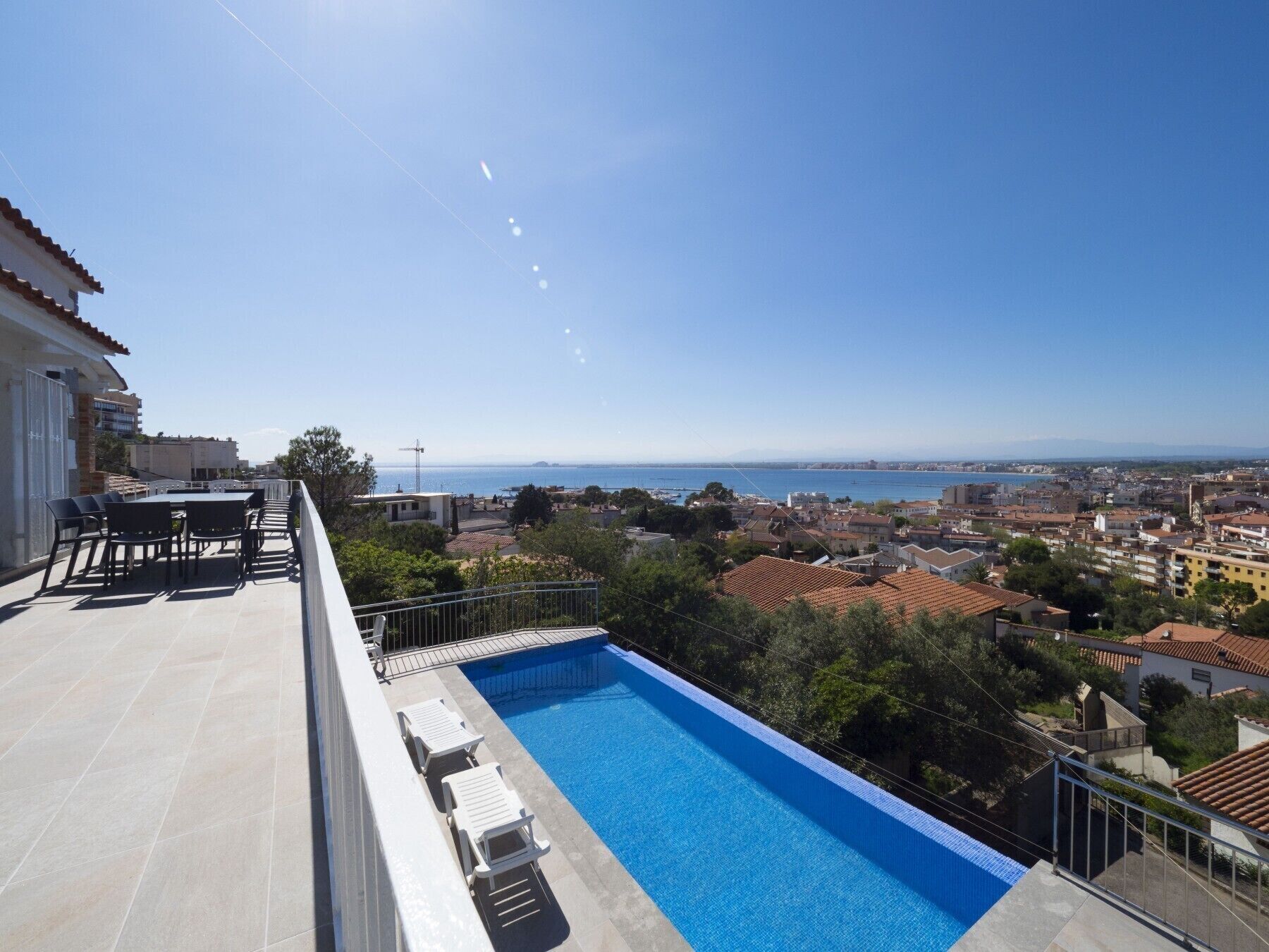 Piscina no terraço com espreguiçadeiras, área de refeições e vista para o mar e a paisagem urbana.