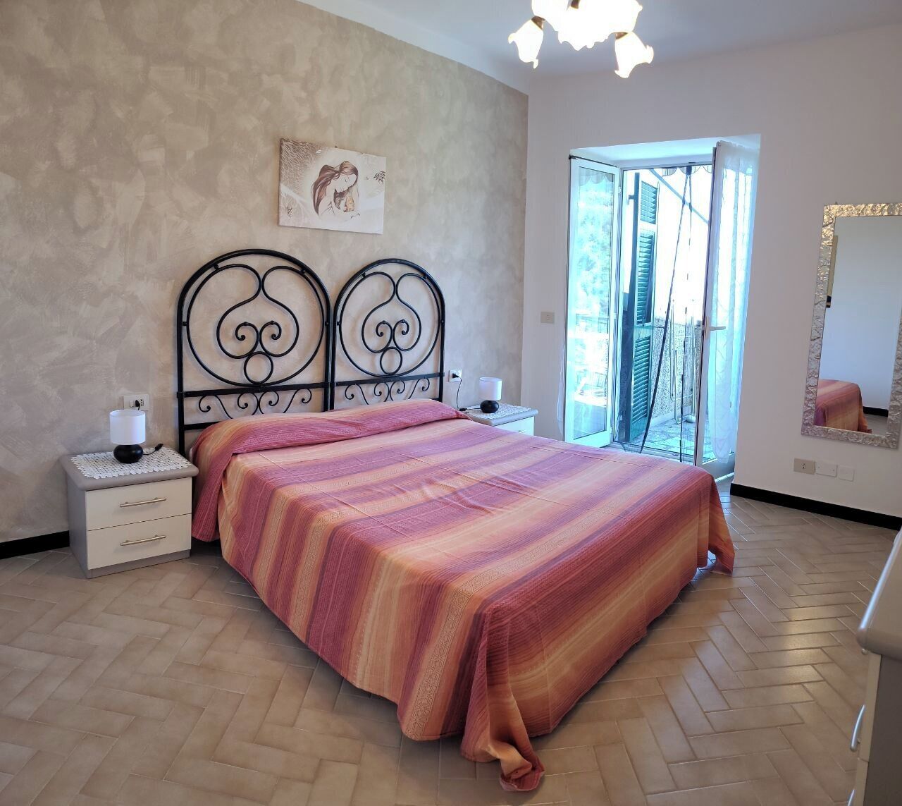 Een slaapkamer met een bed, nachtkastjes, een spiegel aan de muur en uitzicht door een glazen deur.