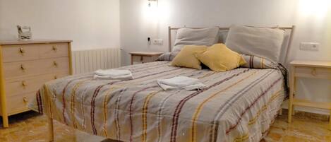 A bedroom with a bed, a dresser, two bedside tables, and a wall-mounted light fixture.