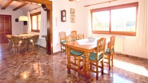 A dining area with a wooden table and chairs, a chandelier, and a large window with curtains. - Calas - Javea, Costa Blanca (Javea)