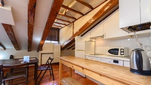 Una cocina con vigas de madera, una mesa de madera, sillas, un microondas y un hervidor.