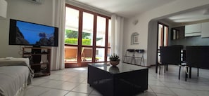 A living room with a TV, a sofa, a coffee table, and a dining area with chairs. - Beautiful house with garden 100 m from the sea. Sinis Regional Park - Montiferru (Torre del Pozzo)
