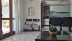 Comedor con una mesa de vidrio, sillas, una planta en maceta y vistas a una cocina.