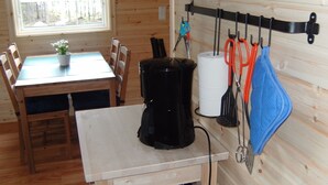 A small kitchen with wooden walls, a table with chairs, a coffee maker, and kitchen utensils hanging on the wall. - Cozy cottage near the lake, including free Wi-Fi and own rowing boat (Hallaryd)
