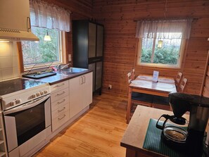 A kitchen with wooden walls, a stove, a sink, and a dining table with chairs.