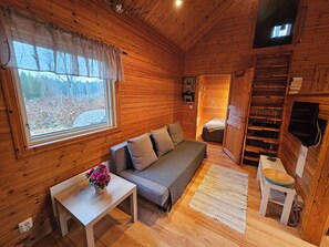 A cozy cabin interior with a sofa, a small table with a vase, a wooden ladder, and a television mounted on the wall.