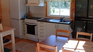 A compact kitchen with a refrigerator, stove, sink, and wooden chairs. - Cozy cottage near the lake, including free Wi-Fi and own rowing boat (Hallaryd)