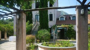 A courtyard with a pergola, a circular garden with plants, and a building with a tiled roof in the background.