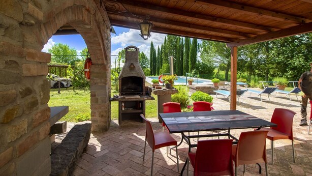 Un patio al aire libre con pared de piedra, horno de ladrillo y mesa con sillas.