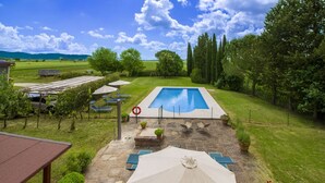 Una piscina con un patio circundante, que incluye sillas de descanso y sombrillas.