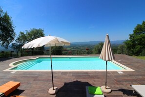 A swimming pool with a view of the landscape, surrounded by patio furniture and umbrellas.