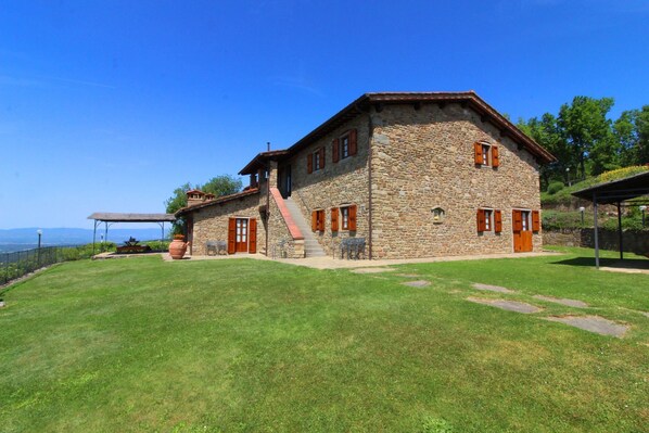 A stone building with a sloped roof, a staircase leading to a second level, and a covered outdoor seating area.