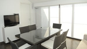 Un comedor moderno con una mesa de vidrio, sillas de mimbre y un televisor de pantalla plana sobre un mueble blanco.
