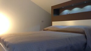 Una cama bien hecha con un edredón acolchado, una mesita de noche y un estante en la pared encima.