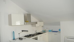 Una cocina moderna con armarios blancos, estufa a gas, pileta y un ventanal.