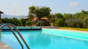 Ein Pool mit einer Metallleiter, umgeben von Grünpflanzen und einem Gebäude mit einem Ziegeldach.