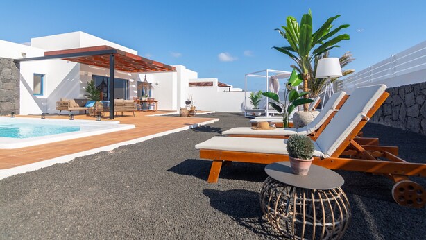 Un espace piscine extérieur moderne, doté de chaises longues, d’une pergola et d’un mur en pierre.