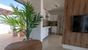 Une cuisine moderne avec des meubles blancs, un réfrigérateur en acier inoxydable et une grande plante en pot.