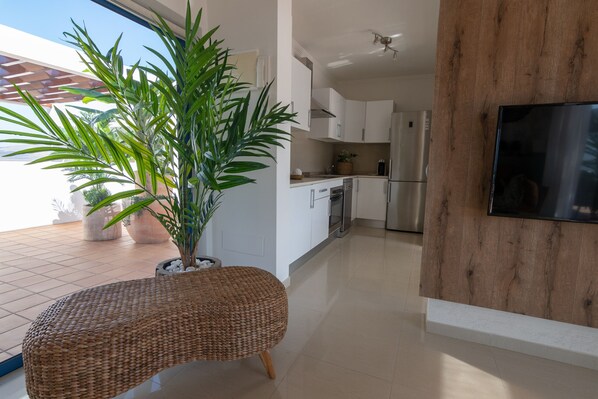 A modern kitchen with white cabinets, a stainless steel refrigerator, and a large potted plant.