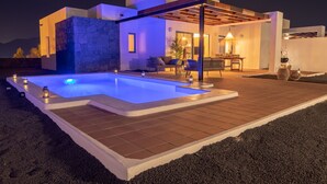 Un espace piscine extérieur moderne, agrémenté d’un mur en pierre, d’une terrasse en bois et de coins salon aménagés sous une pergola.