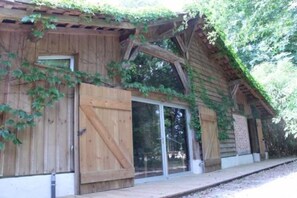 Een rustiek houten gebouw met grote schuifdeuren van glas en een overdekt terras.