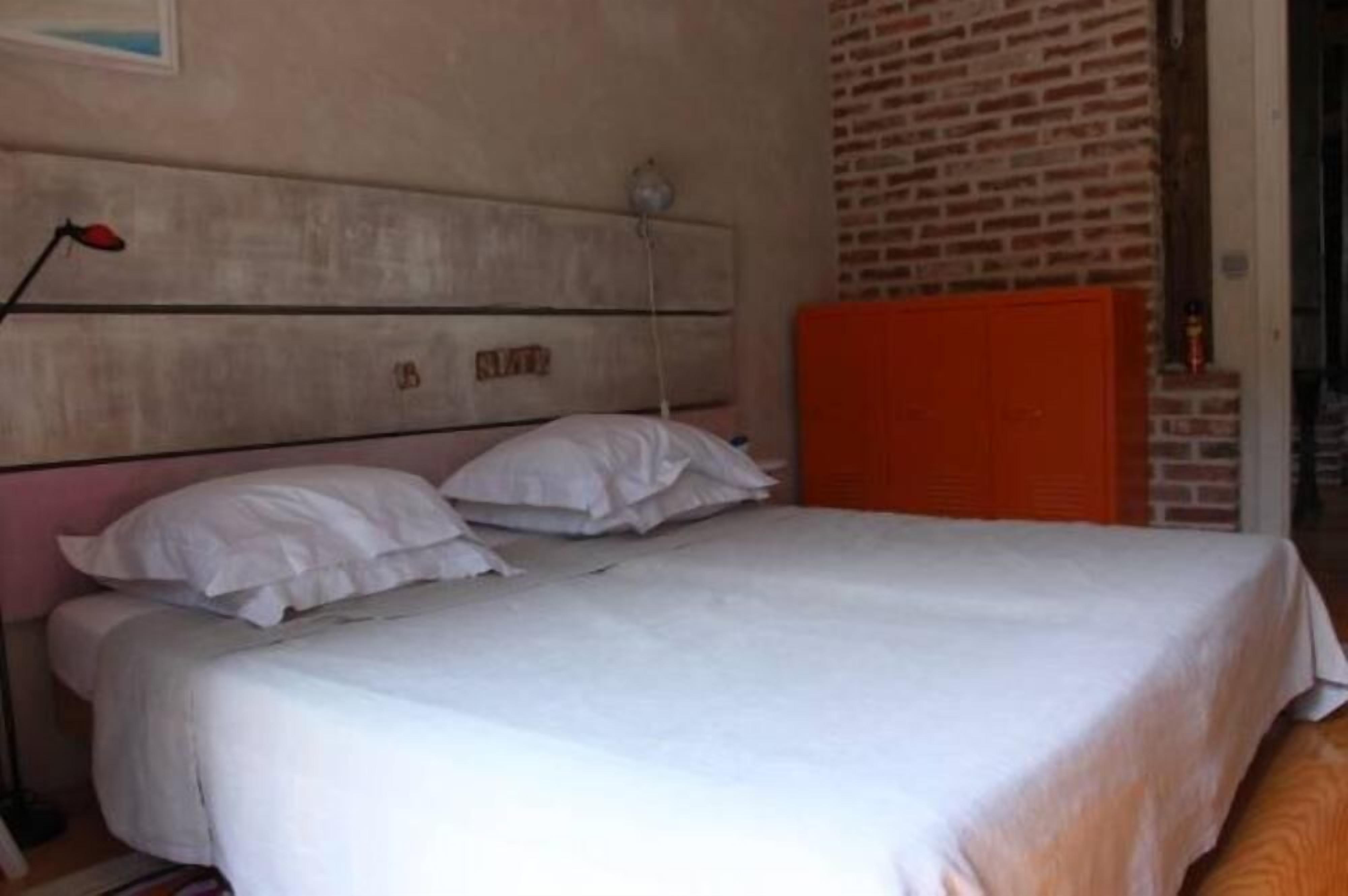 Ein Schlafzimmer mit Bett, weißer Bettwäsche, einem Kopfteil, einem roten Schrank und einer Ziegelwand.