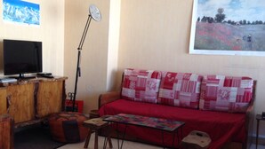 A living room with a red sofa, a wooden coffee table, a television, and a painting on the wall. - Apartment in residence at the foot of the slopes in Tignes Lac promotion 11/18:02 (Tignes)