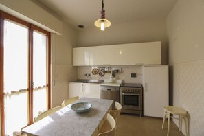 Cocina compacta con mesa, sillas, refrigerador, horno y lámpara colgante.