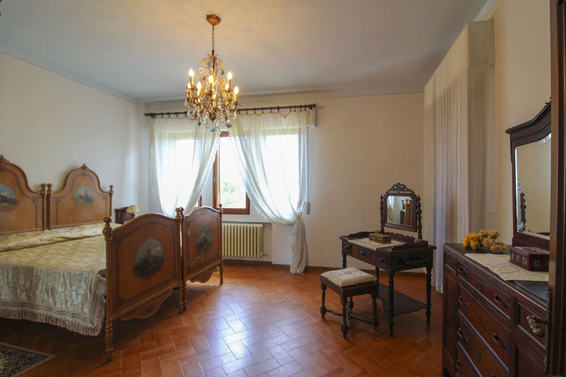 A bedroom with a wooden bed, a dresser, a desk, a mirror, and a chandelier.