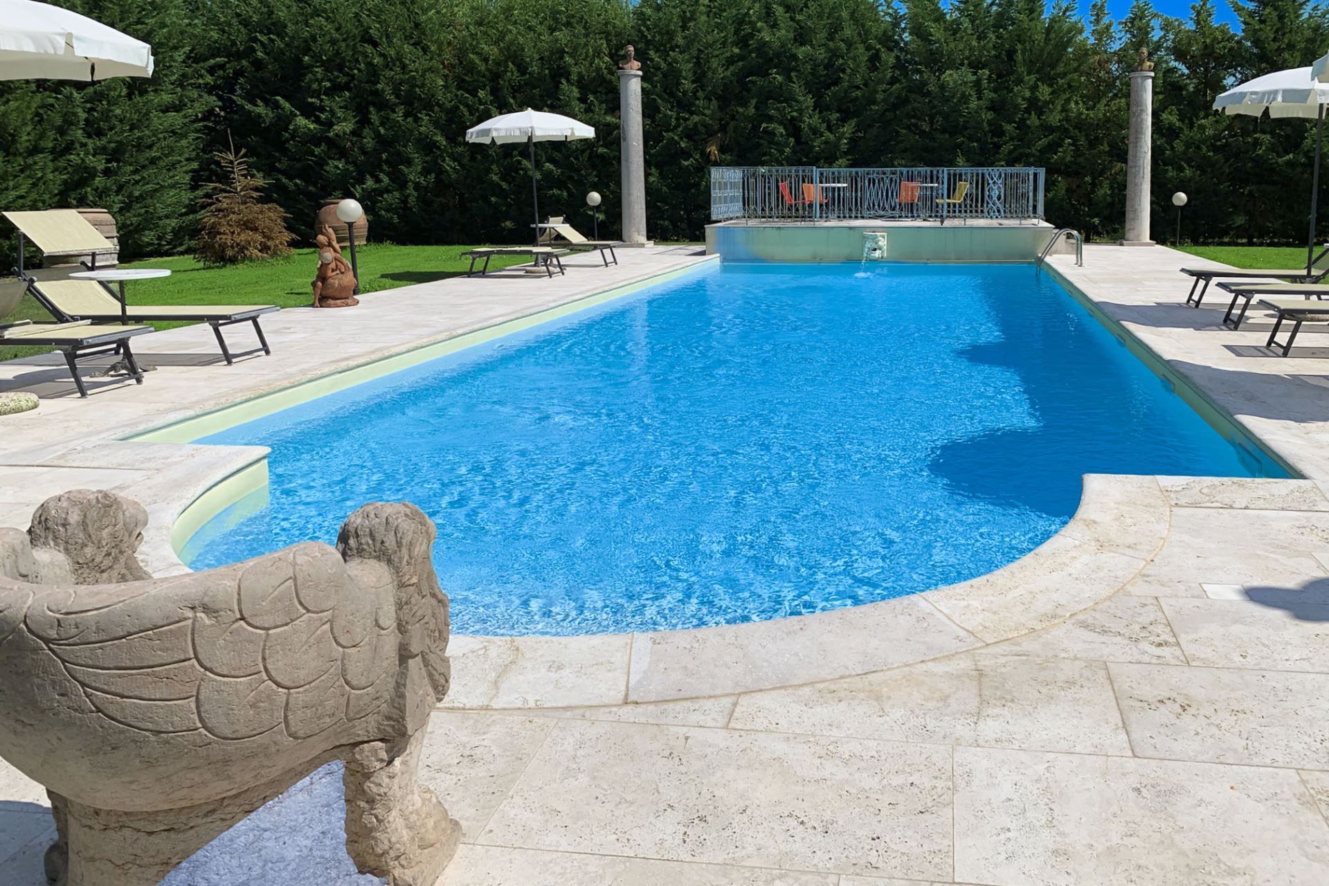 A swimming pool with a stone sculpture in the foreground, surrounded by lounge chairs and umbrellas.