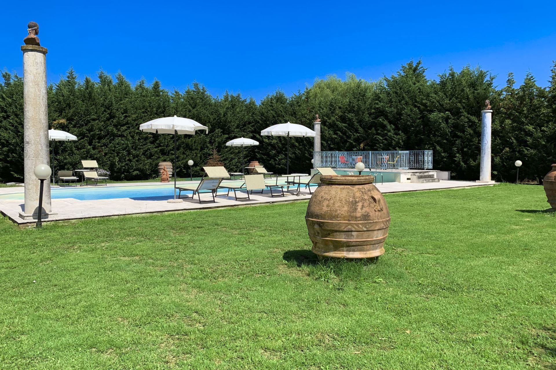 A pool area with lounge chairs, umbrellas, and a large urn.