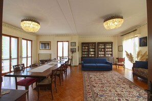 A spacious living room with a large wooden dining table, blue sofa, and two chandeliers.