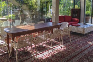 Une pièce spacieuse avec une grande table en bois, entourée de chaises en osier, d’un canapé rouge et d’un tapis à motifs.