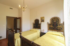 A bedroom with two beds, a chandelier, a door, and a painting on the wall.