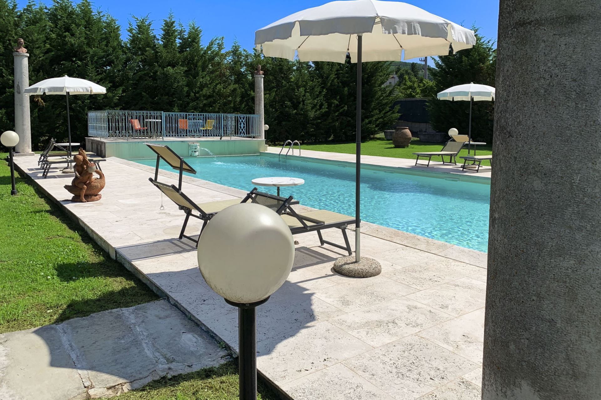 Un espace piscine doté de chaises longues et de parasols, entouré de verdure.