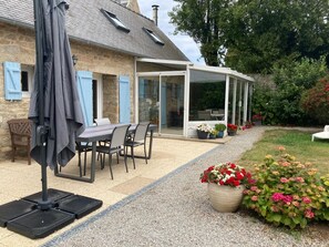 Un patio cubierto con mesa y sillas, una sombrilla y un jardín con flores.