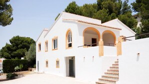 A two-story white house with a tiled roof, a staircase leading to the entrance, and a small garden area. - Caleta - Javea, Costa Blanca (Javea)