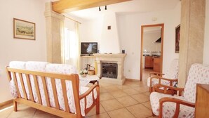 A living room with a fireplace, wooden furniture, and a television. - Caleta - Javea, Costa Blanca (Javea)