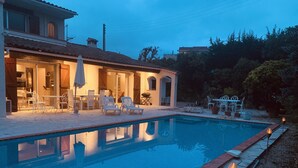 Ein Pool mit Liegestühlen und Sonnenschirmen, umgeben von einer Terrassenanlage, im Hintergrund ein Haus.