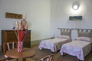Une chambre avec deux lits, une commode en bois, une table avec des chaises et un luminaire fixé au mur.