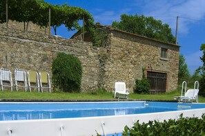 A stone building with a pool, white lounge chairs, and a small garden area.