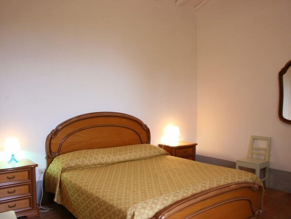 A bedroom with a wooden bed, a nightstand with a lamp, a dresser, and a small table with a chair. - Country house with an original tower dating back to 1500. In a panoramic position, surrounded by vin (Capolona)