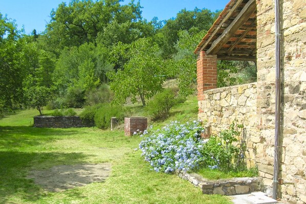 Un bâtiment en pierre avec une extension en briques, entouré d’une zone herbeuse et d’arbres.