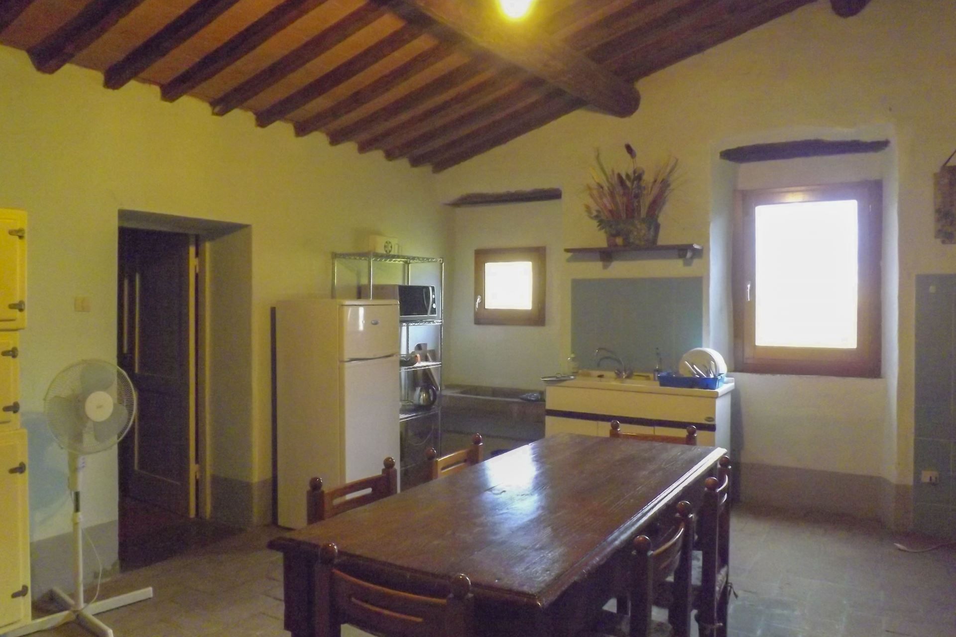 A kitchen with a wooden table, chairs, a refrigerator, a fan, and a window.