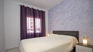 A bedroom with a bed, a nightstand, a lamp, and a window with purple curtains. - Nice apartment in front of the sea in Roses Inmosantos Oasis E3 (Rosas / Roses)